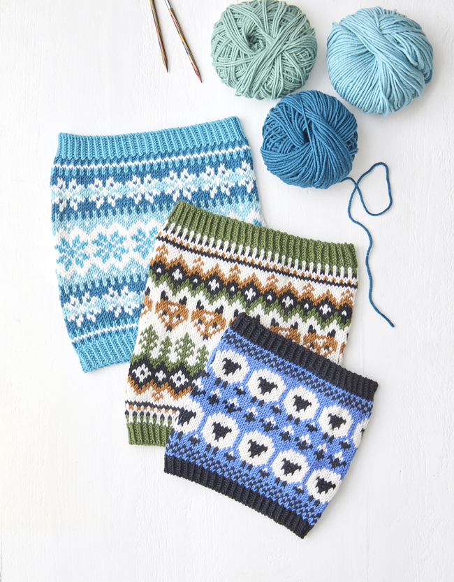 Trois cols tricotés en jacquard aux motifs géométriques, accompagnés de pelotes de laine dans des tons bleu et vert.