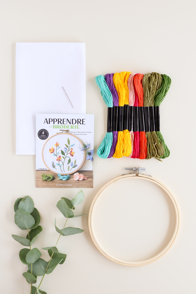 Kit pour apprendre la broderie avec tambour à broder, fils colorés, aiguille, toile blanche et livret explicatif pour réaliser des motifs floraux.