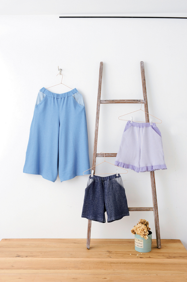 Ensemble de vêtements enfant comprenant jupe, short et pantalon suspendus sur une échelle décorative, idéal pour couture DIY, mode enfant et créations textiles faites main.