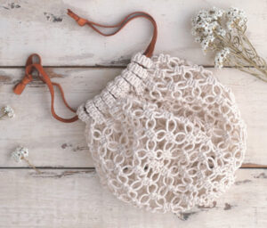 Pochette filet crochetée couleur écru avec cordon en cuir, posée sur table en bois avec fleurs séchées, accessoire artisanal idéal pour crochet DIY, mode bohème et créations faites main