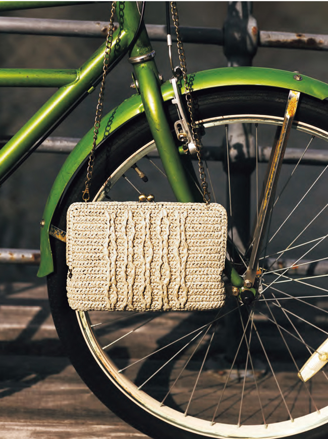 Pochette rectangulaire en raphia crocheté suspendue à un vélo vert, création artisanale idéale pour crochet DIY, accessoires de mode, sac fait main et style bohème chic.