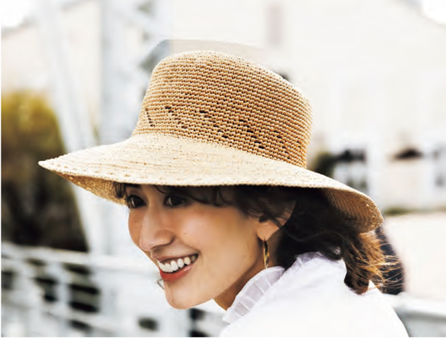 Femme souriante portant un chapeau en raphia tressé à large bord, accessoire estival élégant idéal pour crochet DIY, mode estivale, accessoires handmade et inspiration vacances.