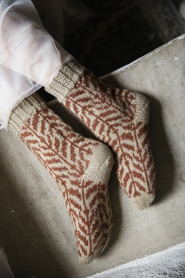 Chaussettes tricotées beige et terracotta ornées de motifs jacquard graphiques, portées aux pieds.