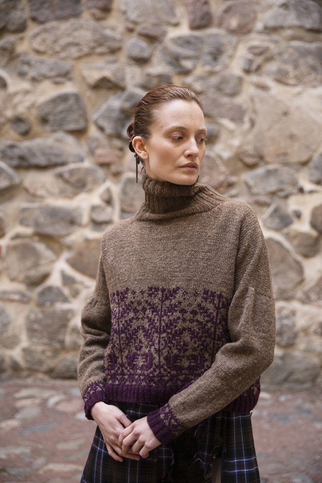 Femme portant un pull en tricot marron à col roulé, orné de motifs jacquard violets sur le bas et les poignets.