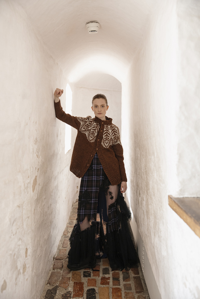 Femme portant un cardigan en tricot marron à motifs jacquard écrus, associé à une longue jupe à carreaux.
