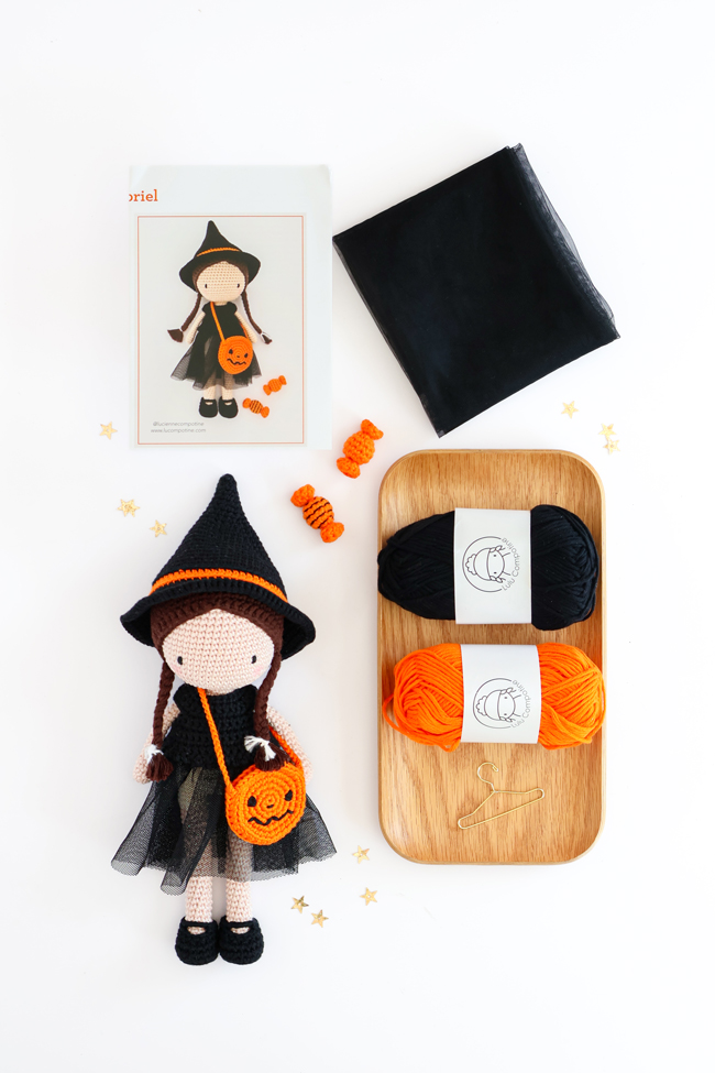 Contenu de la panoplie Lulu au bal des sorcières de Sandra Muller (Lulu Compotine) : poupée au crochet vêtue d'un costume de sorcière, pelotes de laine, tissu noir, mini-cintre et livret d'instructions, présenté sur fond blanc.