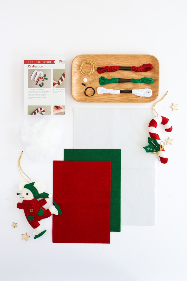 Contenu du kit créatif Sucre d'orge : feutrine rouge, verte et blanche, fils à broder, rembourrage, cordon, accessoires de montage, tutoriel pas à pas et suspensions sucre d'orge et lutin, présenté sur fond blanc.