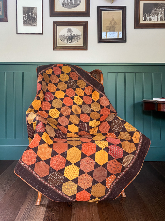 Plaid en patchwork aux motifs géométriques dans des tons orange, ocre et marron, présenté sur un fauteuil