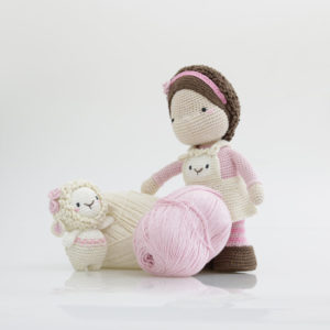 Poupée amigurumi crochetée assise avec pelote de laine rose et petit mouton, ambiance douce et créative idéale pour crochet DIY, loisirs créatifs et créations faites main