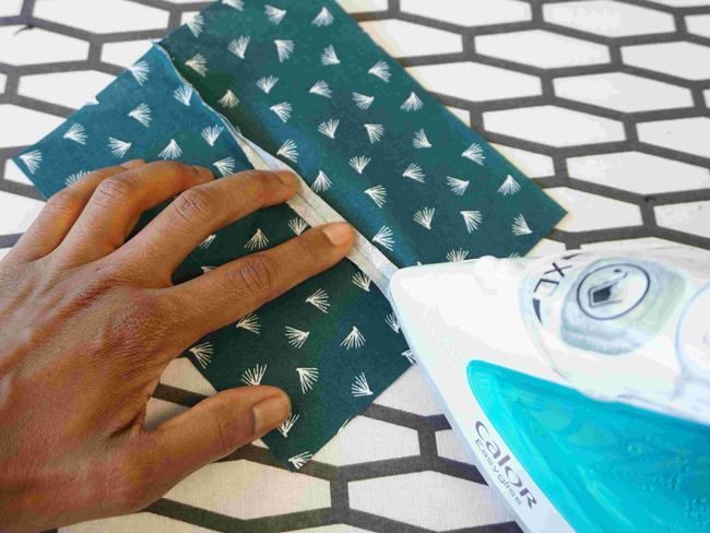 Main repassant un tissu imprimé bleu avec un fer à repasser, étape de préparation couture DIY idéale pour confection textile, création de vêtements et loisirs créatifs couture maison