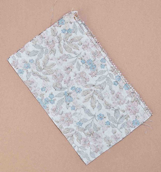 Échantillon de tissu fleuri avec couture de finition visible sur fond beige, étape de confection textile idéale pour couture DIY, apprentissage couture, création de vêtements et loisirs créatifs textiles