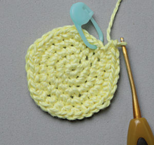 Petit cercle crocheté jaune avec marqueur de maille et crochet, étape de réalisation d’un amigurumi ou d’un projet au crochet, idéal pour tutoriel crochet DIY, apprentissage des techniques de base et loisirs créatifs textile