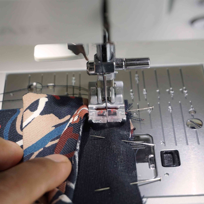Gros plan sur une machine à coudre assemblant un tissu imprimé avec épingles visibles, idéal pour couture DIY, confection textile, loisirs créatifs et apprentissage de la couture maison