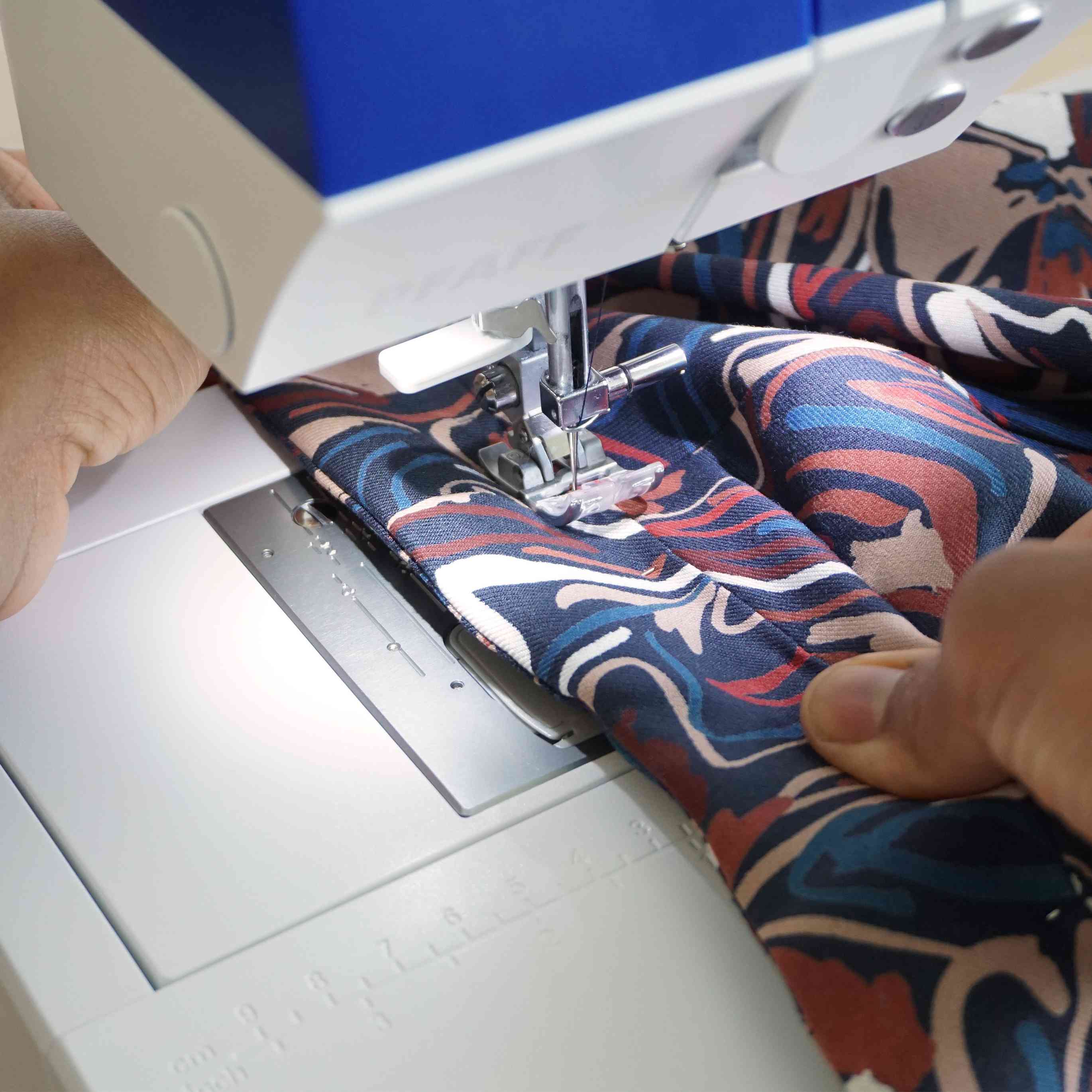 Machine à coudre assemblant un tissu imprimé aux motifs colorés, gros plan sur une étape de confection textile, idéal pour couture DIY, création de vêtements, apprentissage couture et loisirs créatifs maison
